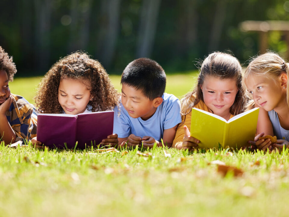 Shot of a group of kids reading a book outside